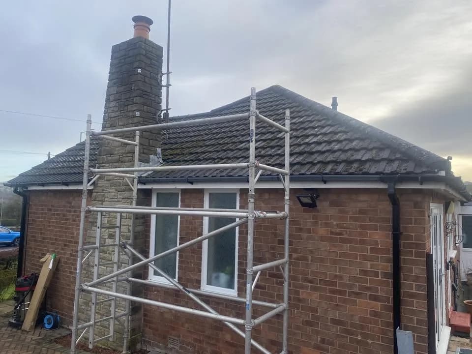 Scaffolded bungalow roofline with black gutters and fascia